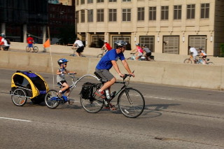 Man with child on tandem bike and in bike trailer